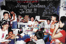 Students & teacher sitting around table in front of chalkboard with artistic Christmas greeting in chalk