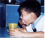 Same boy happily eating large spoonful of food.