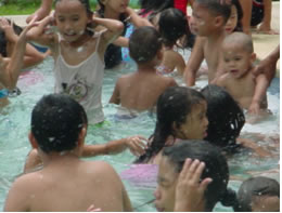 Large number of children splashing and having fun in a pool.