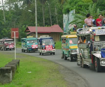 Colorful jeepney Busses traveling single file down a road.